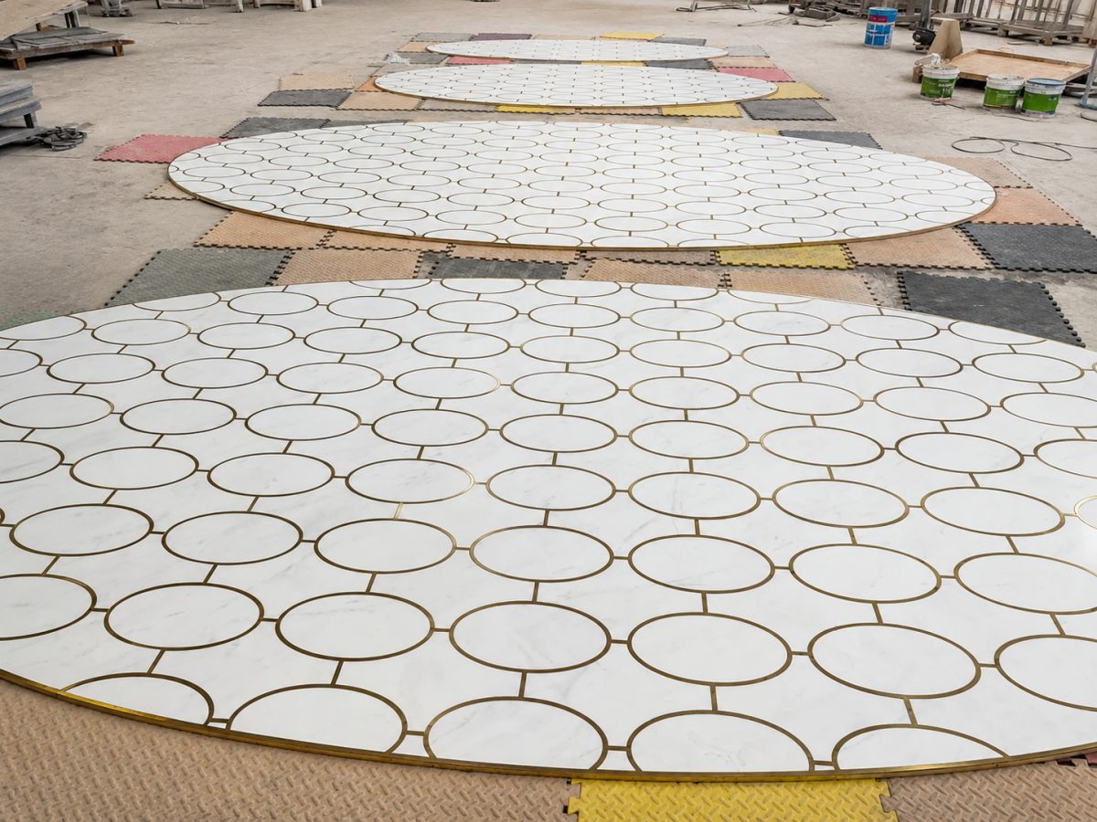 marble-medallion-factory-preassembly-inspection Multiple white marble floor medallion sections with brass inlay laid out for factory inspection